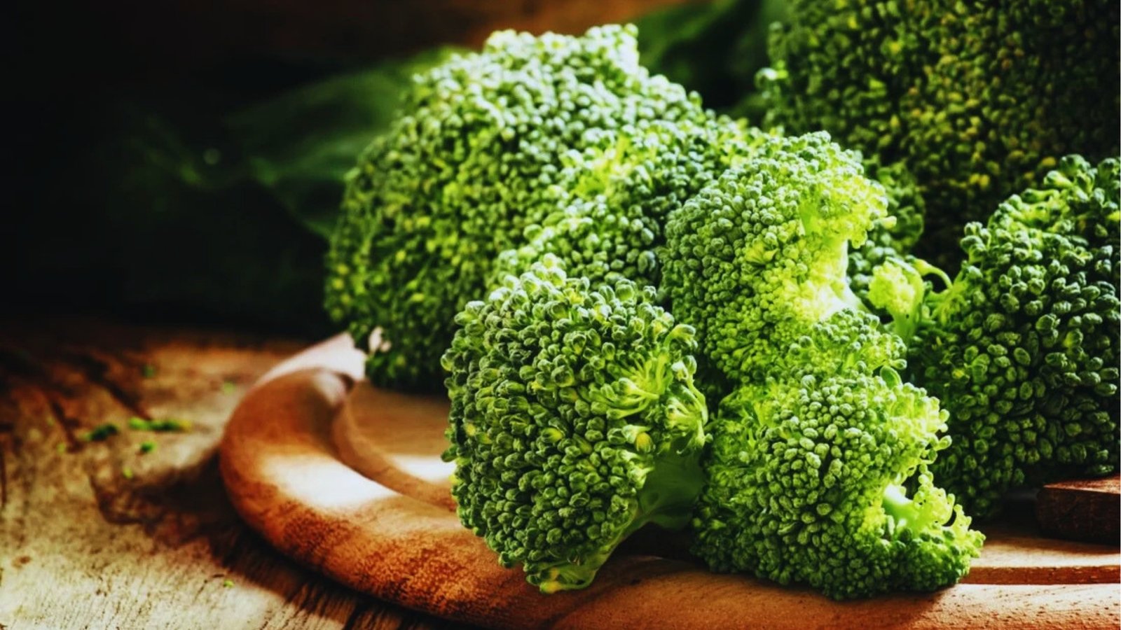 Close-up of several fresh broccoli crowns with tight green florets arranged on rustic wooden cutting boards.
