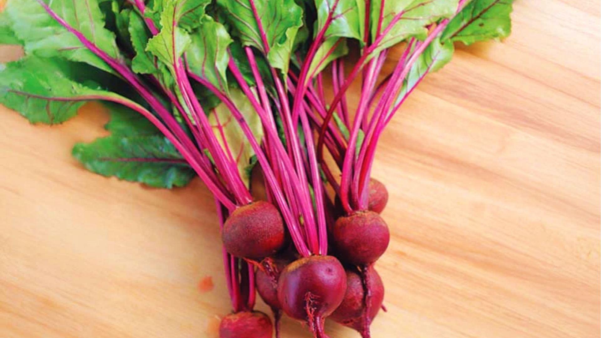 Bunch of Merlin beets with vibrant magenta stems and green leaves on a light wood surface.