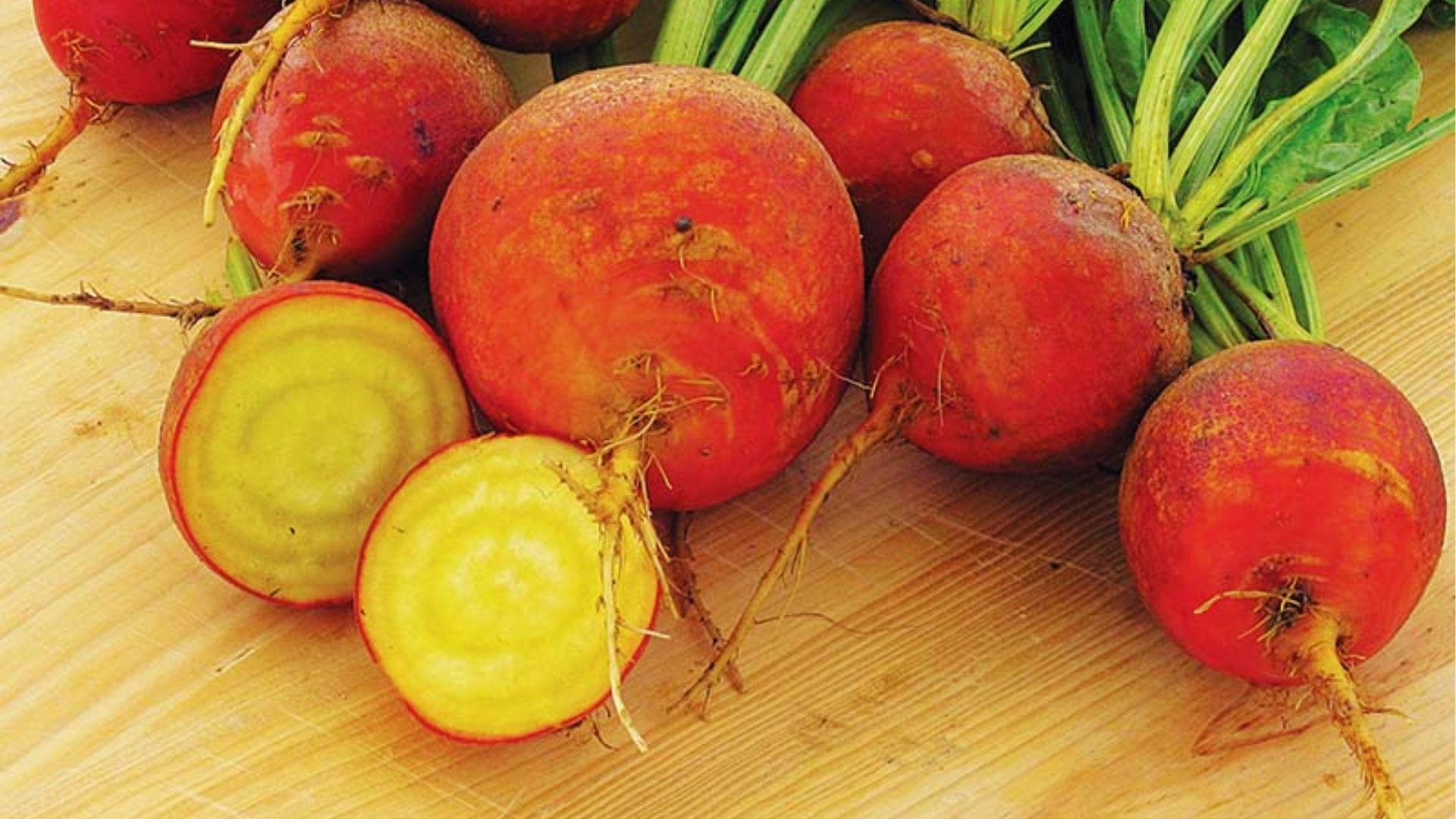 Bunch of Touchstone golden beets with red skin and pale yellow rings inside, halved on a wooden table.