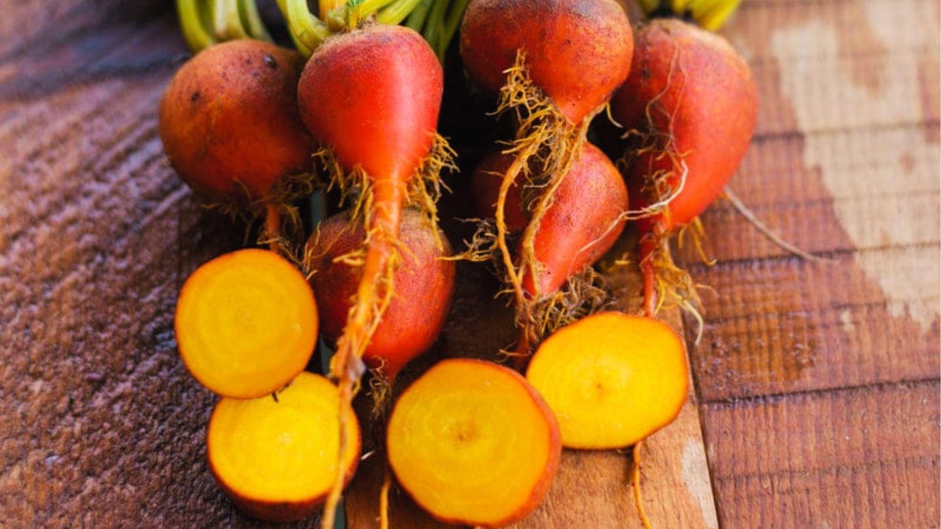 Fresh golden beets with orange-red skin and sunny yellow interior, sliced on rustic wood background.