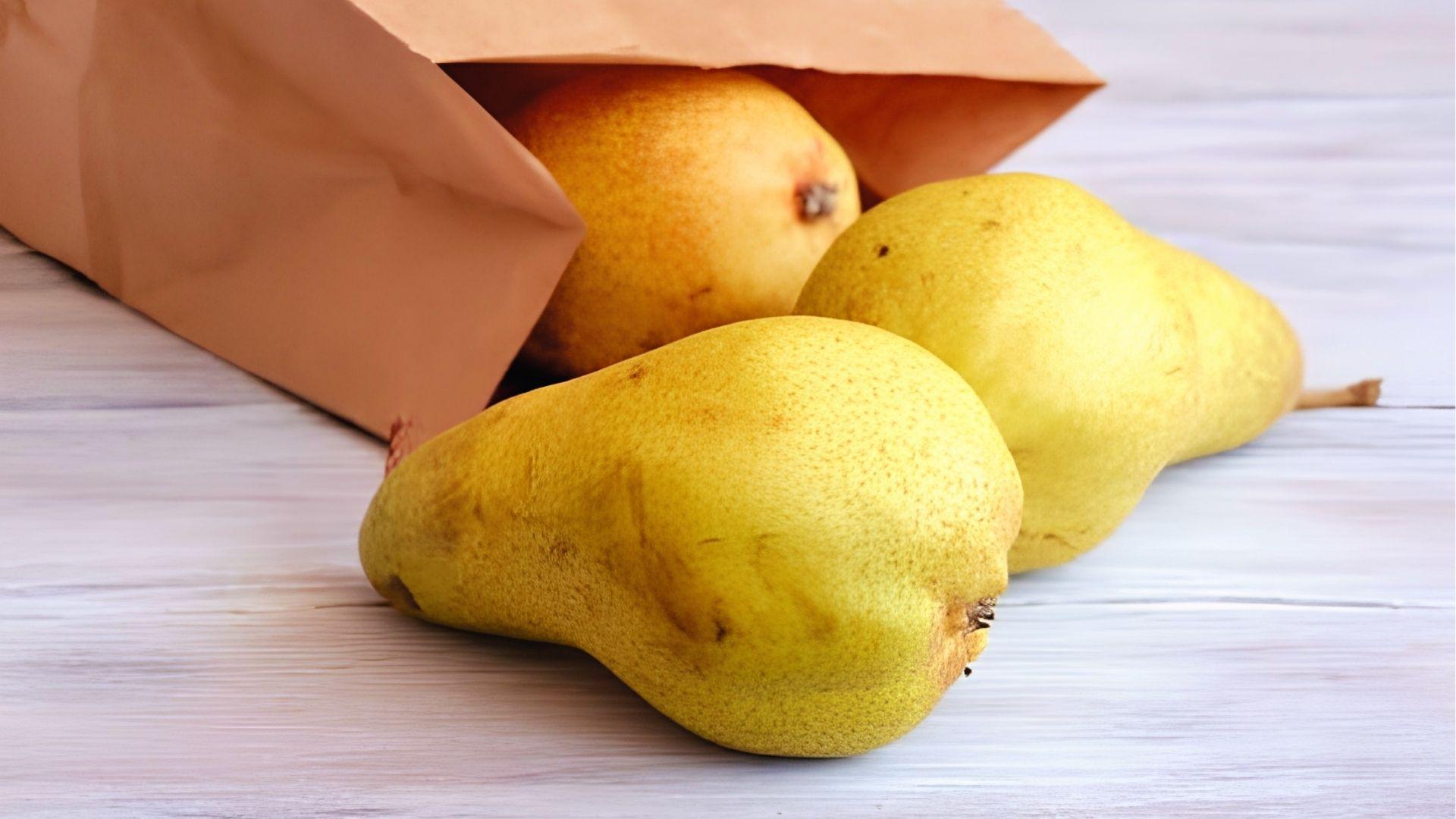 Ripe yellow pears spill from a paper bag. Harvest pears when skin lightens but fruit is still firm.