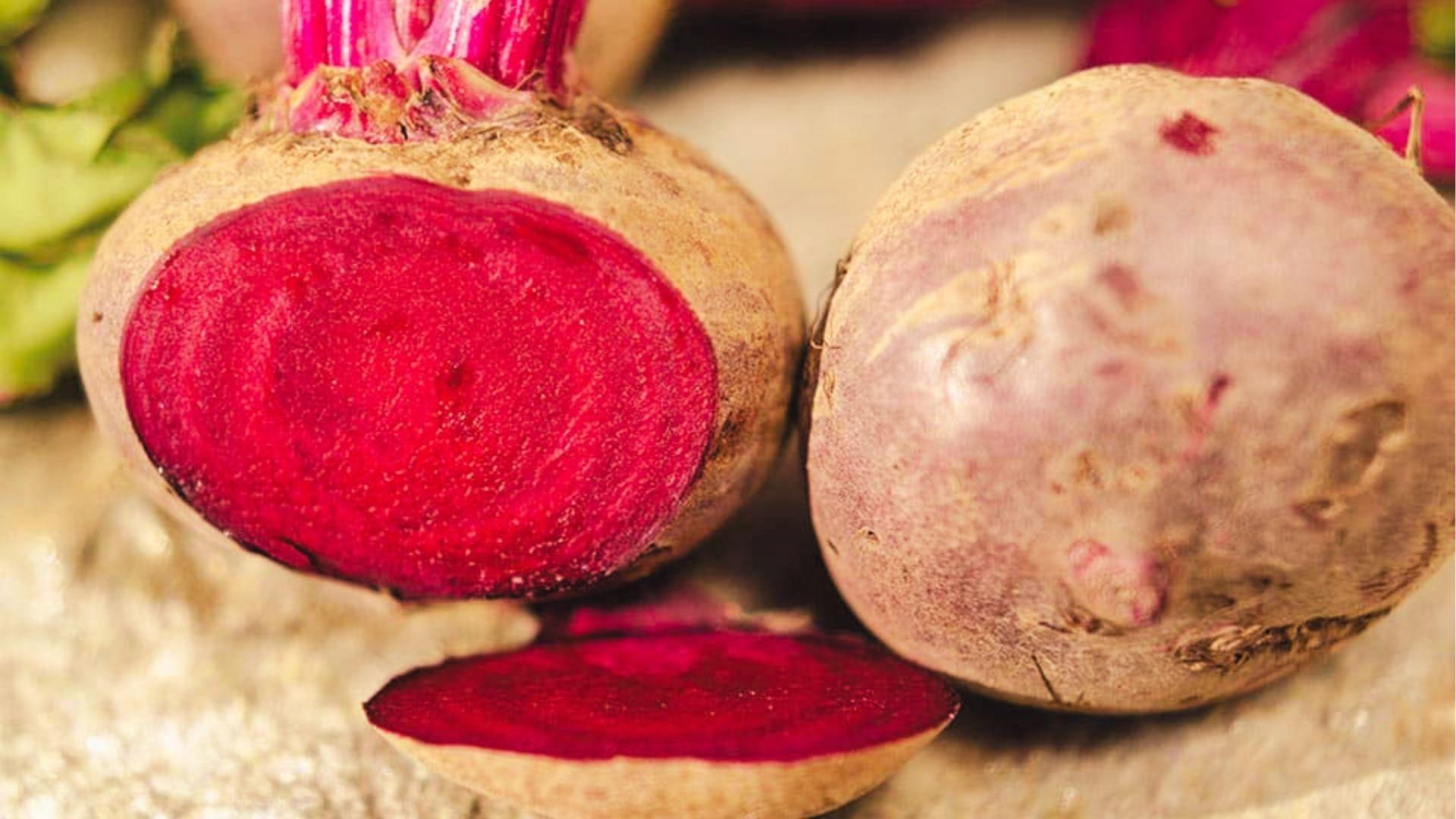 Halved red beet revealing vibrant magenta interior next to whole beet with pale brown skin and pink stem.