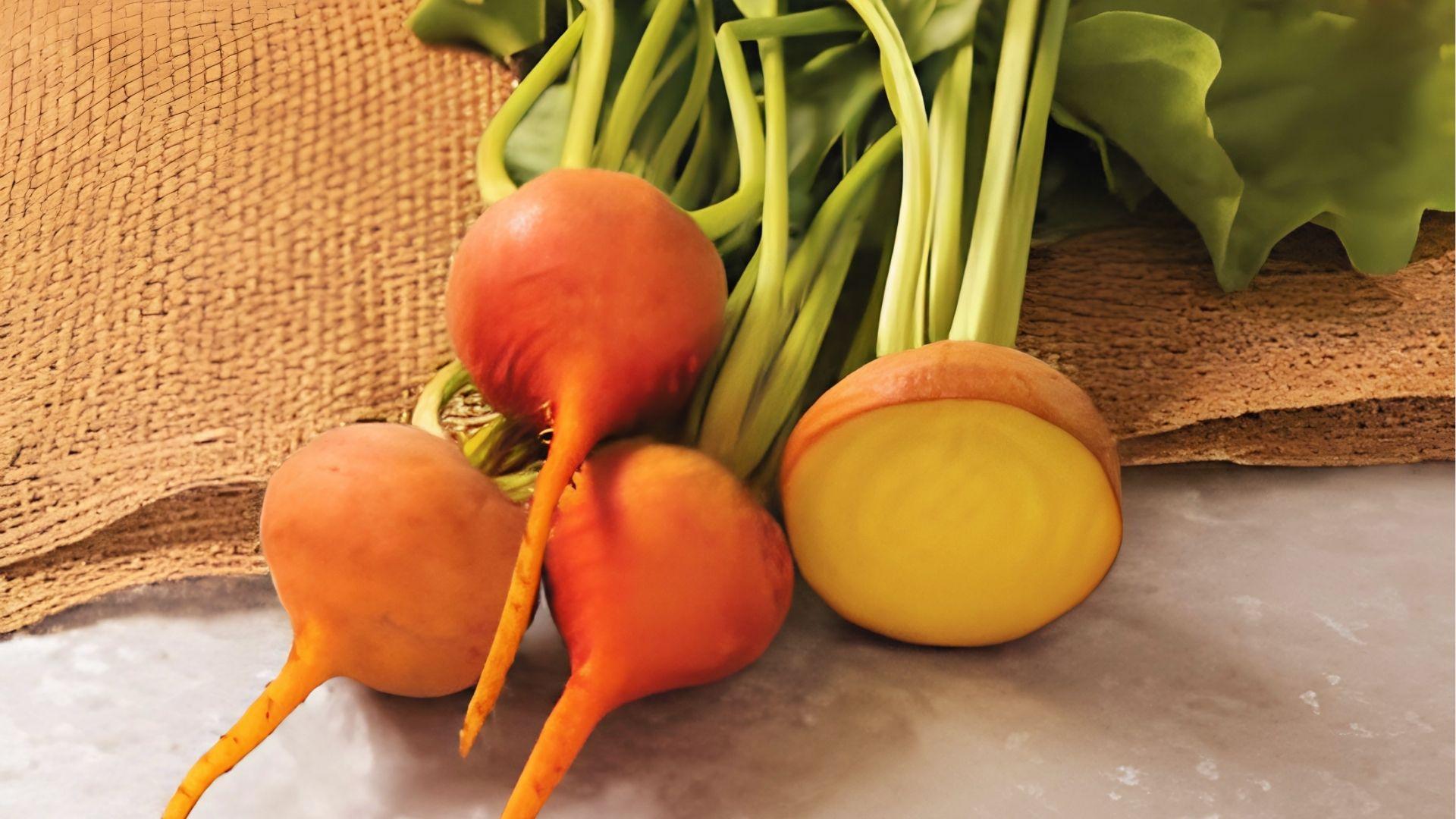 Boldor beets with orange skin and bright yellow flesh, one cut open, on burlap with green tops.