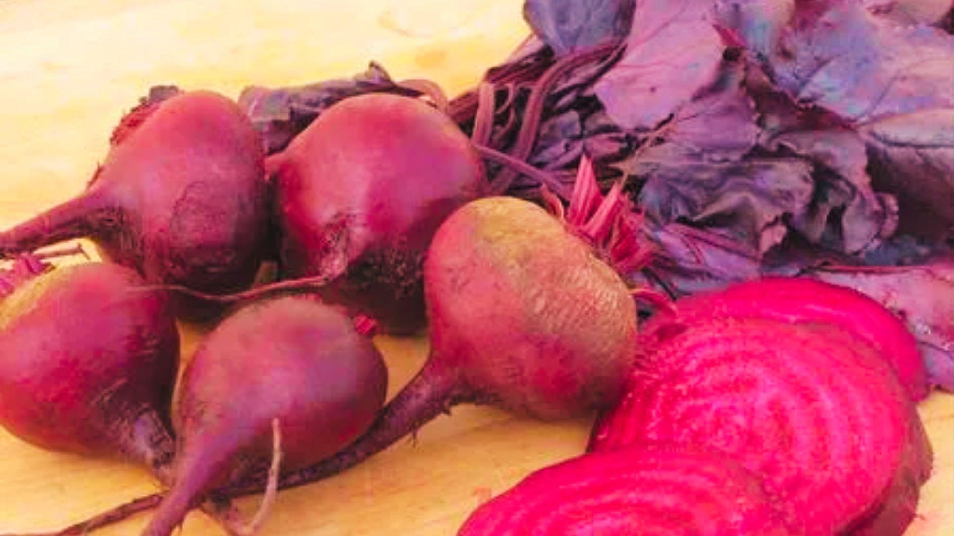 Sliced red beets on wood board showing deep crimson flesh with purple leaves, classic beet type.