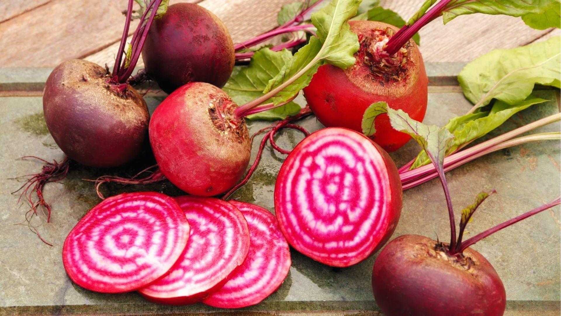 Whole and sliced Chioggia beets showing striking pink and white candy-stripe rings on the stone surface.