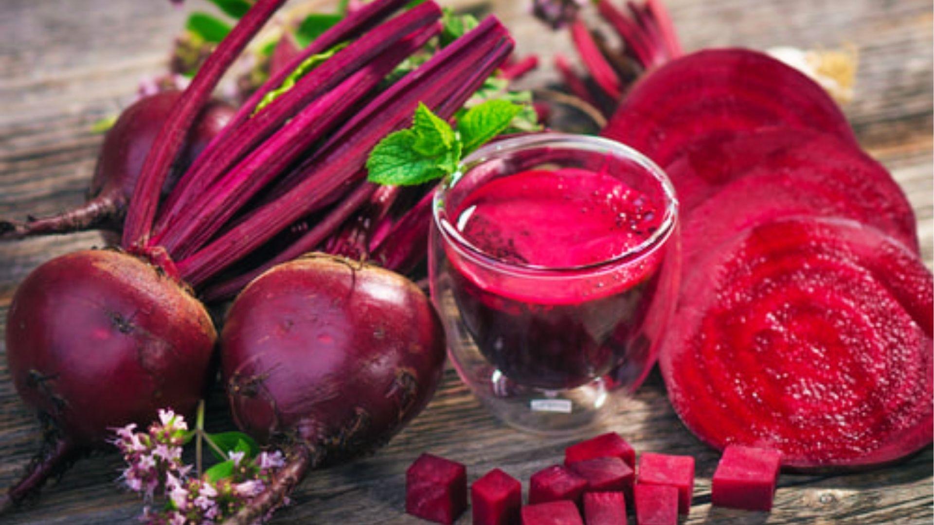 Whole and sliced red beets showing deep ruby flesh and earthy skin on rustic wood with mint leaves.